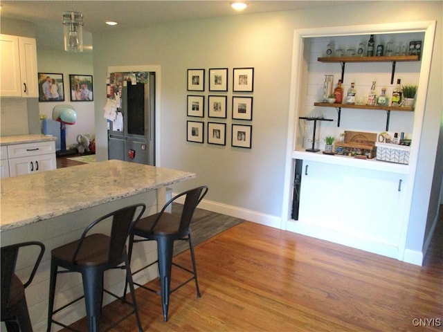7739 Roberts St, Lenox, NY 13032 - kitchen with white cabinets, a breakfast bar area, fridge, wood finished floors, and recessed lighting