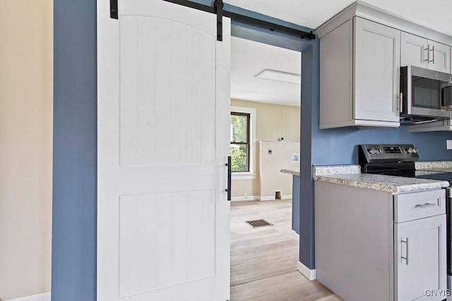 81 E 10th St, Oswego, NY 13126 - kitchen featuring stainless steel appliances, a barn door, light countertops, and light wood-style floors