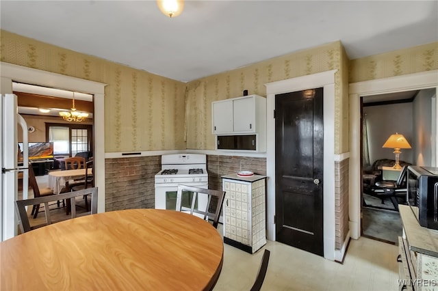 53 Pine Rdg, Cheektowaga, NY 14225 - kitchen featuring white gas range oven, wallpapered walls, light flooring, a chandelier, and white cabinets