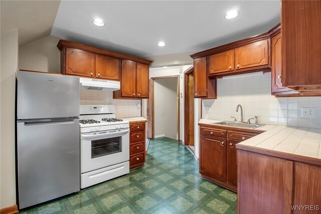 74 Bush St, Buffalo, NY 14207 - kitchen with freestanding refrigerator, white range with gas cooktop, under cabinet range hood, dark floors, and tile counters