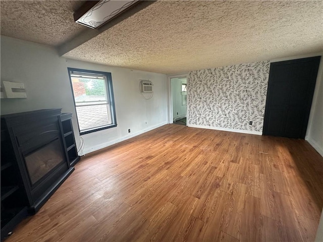 8557 Reeds Corners Rd, Sparta, NY 14437 - unfurnished living room featuring a textured ceiling, wood finished floors, an AC wall unit, and wallpapered walls