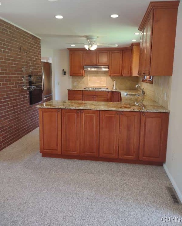 7408 Rome Oriskany Rd, Rome, NY 13440 - kitchen featuring under cabinet range hood, light stone countertops, brown cabinetry, brick wall, and recessed lighting