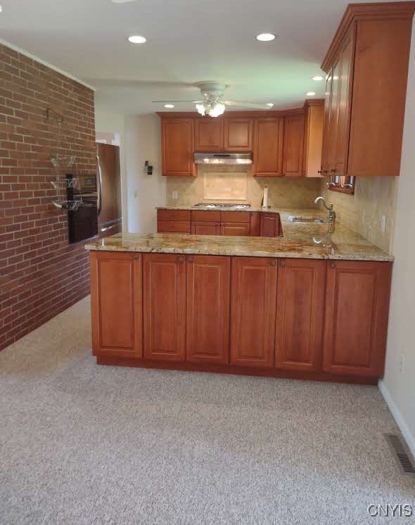 7408 Rome Oriskany Rd, Rome, NY 13440 - kitchen featuring under cabinet range hood, stainless steel appliances, light stone counters, brown cabinetry, and a peninsula