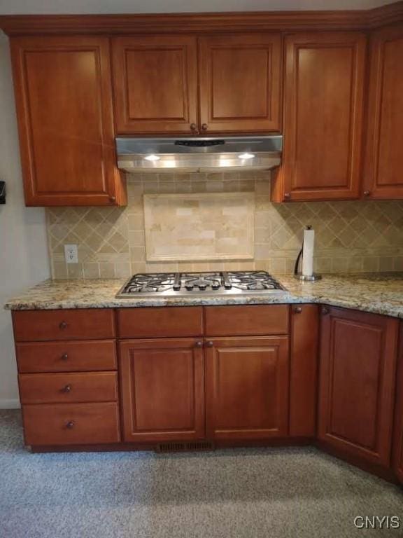 7408 Rome Oriskany Rd, Rome, NY 13440 - kitchen with under cabinet range hood, stainless steel gas cooktop, light stone counters, backsplash, and brown cabinets