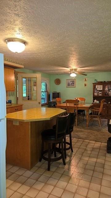 8198 Rte 46, Keating Town, PA 16749 - kitchen with freestanding refrigerator, a textured ceiling, light countertops, a kitchen breakfast bar, and light tile patterned floors