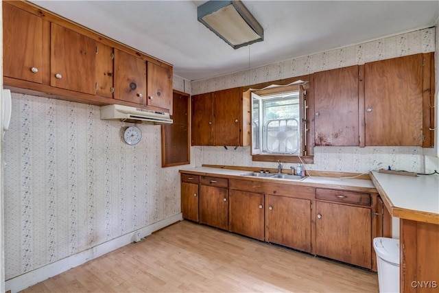 7259 Number Four Rd, Watson, NY 13367 - kitchen with wallpapered walls, brown cabinetry, under cabinet range hood, light wood-type flooring, and light countertops