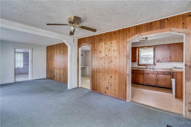 7259 Number Four Rd, Watson, NY 13367 - unfurnished living room featuring arched walkways, wooden walls, a ceiling fan, light carpet, and a textured ceiling