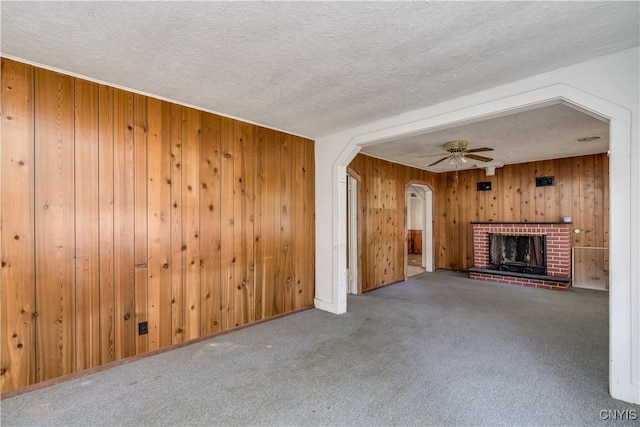7259 Number Four Rd, Watson, NY 13367 - unfurnished living room with arched walkways, wooden walls, a textured ceiling, carpet, and a fireplace