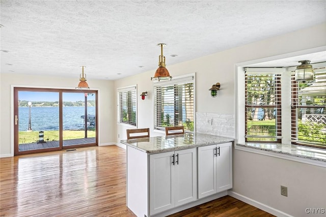 2761 E Lake Rd, Skaneateles, NY 13152 - kitchen with wood finished floors, light stone countertops, a peninsula, hanging light fixtures, and a textured ceiling