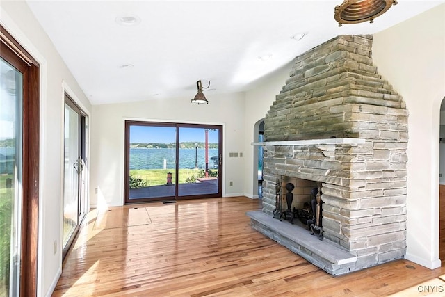 2761 E Lake Rd, Skaneateles, NY 13152 - unfurnished living room with vaulted ceiling, a stone fireplace, light wood-style floors, arched walkways, and a water view