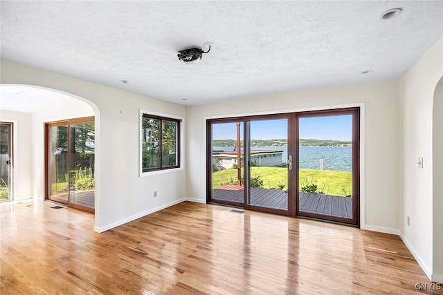 2761 E Lake Rd, Skaneateles, NY 13152 - spare room with arched walkways, a water view, light wood-style floors, and a textured ceiling