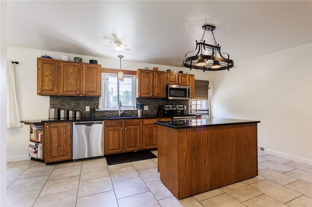 304 Simpson Rd, Irondequoit, NY 14617 - kitchen featuring stainless steel appliances, tasteful backsplash, dark countertops, brown cabinetry, and hanging light fixtures