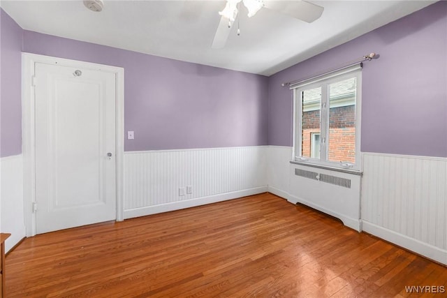 711 Colvin Blvd, Tonawanda, NY 14217 - unfurnished room featuring radiator heating unit, a wainscoted wall, wood finished floors, a ceiling fan, and a smoke detector