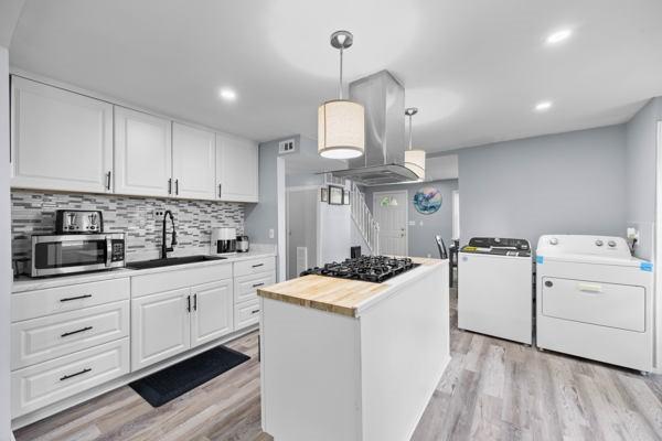 95 Ridgemar Rd, Greece, NY 14615 - kitchen with stainless steel microwave, black stovetop, washer and clothes dryer, light wood-type flooring, and white cabinetry