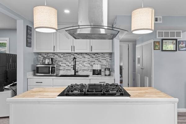 95 Ridgemar Rd, Greece, NY 14615 - kitchen with exhaust hood, black gas stovetop, stainless steel microwave, backsplash, and white cabinetry