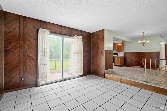 270 N French Rd, Amherst, NY 14228 - unfurnished living room featuring wood walls, a chandelier, a textured ceiling, light tile patterned flooring, and wainscoting