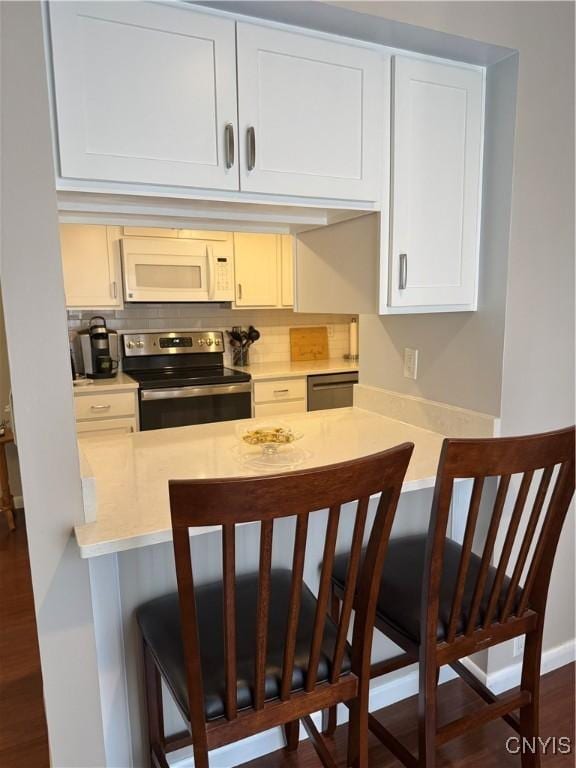 601 Woburn Dr, Camillus, NY 13031 - kitchen featuring stainless steel appliances, light countertops, a kitchen bar, a peninsula, and dark wood-style flooring