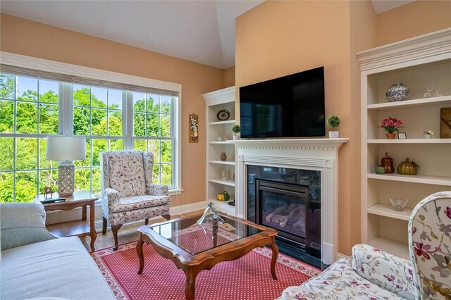 1100 Yorkshire Way, Victor, NY 14564 - living room featuring built in shelves, lofted ceiling, a glass covered fireplace, and wood finished floors