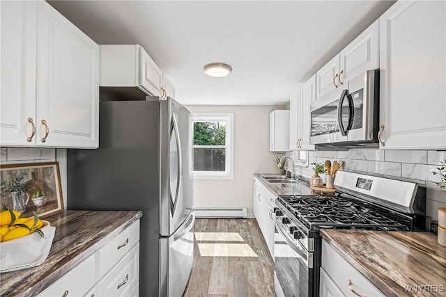 87 Ermann Dr, Tonawanda, NY 14217 - kitchen featuring stainless steel appliances, baseboard heating, wood finished floors, dark countertops, and backsplash