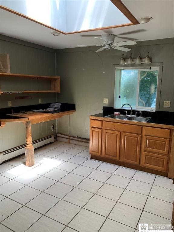 749-753 W Main, Ellington, NY 14732 - kitchen with brown cabinets, light tile patterned flooring, ceiling fan, dark countertops, and a baseboard radiator