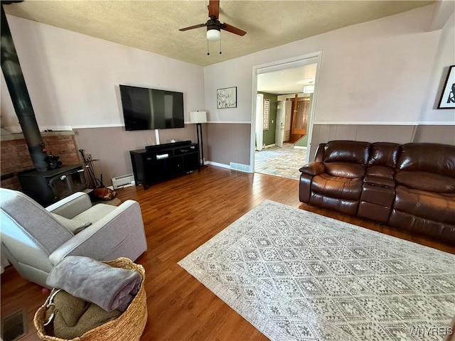 80 Fredro St, Buffalo, NY 14206 - living room with a ceiling fan, a wainscoted wall, wood finished floors, a baseboard radiator, and a wood stove