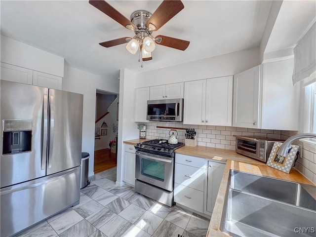 8 Harnden St, Auburn, NY 13021 - kitchen featuring stainless steel appliances, white cabinetry, a ceiling fan, tasteful backsplash, and light marble finish floors