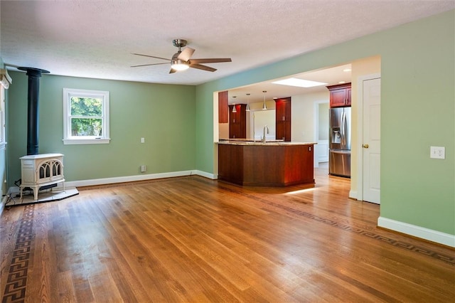 179 Down St, Henrietta, NY 14623 - unfurnished living room with ceiling fan, wood finished floors, a wood stove, and a textured ceiling