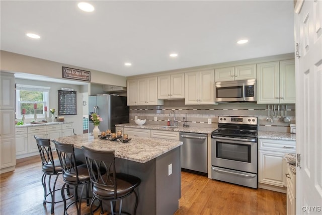 4956 Crestwood Ln, Onondaga, NY 13215 - kitchen featuring appliances with stainless steel finishes, a breakfast bar area, decorative backsplash, light stone countertops, and a center island