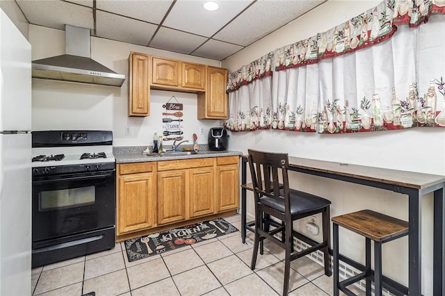 1570 Mount Hope Ave, Rochester, NY 14620 - kitchen featuring wall chimney range hood, gas range oven, light tile patterned floors, freestanding refrigerator, and a drop ceiling