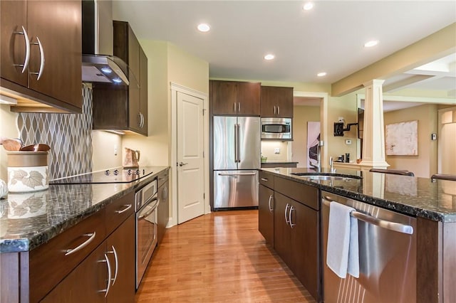 1537 Cranberry Pond, Victor, NY 14564 - kitchen featuring stainless steel appliances, wall chimney exhaust hood, ornate columns, light wood-style floors, and dark stone counters