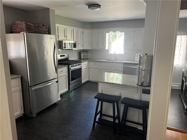 78 Falleson Rd, Rochester, NY 14612 - kitchen featuring appliances with stainless steel finishes, white cabinets, tasteful backsplash, light stone countertops, and a kitchen breakfast bar