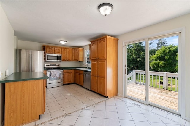 1535 Bluestem Ct, Walworth, NY 14568 - kitchen featuring stainless steel appliances, dark countertops, brown cabinets, and light tile patterned floors