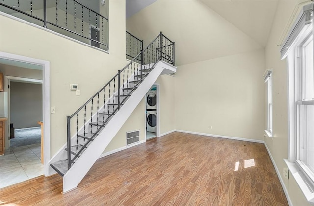 1162 Draper Ave, Elmira, NY 14905 - unfurnished living room featuring estacked washer and dryer, high vaulted ceiling, stairs, wood finished floors, and healthy amount of natural light