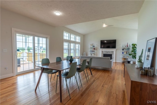 3427 Tall Tree Ln, Lysander, NY 13027 - dining space featuring light wood-type flooring, a fireplace, lofted ceiling, and a ceiling fan