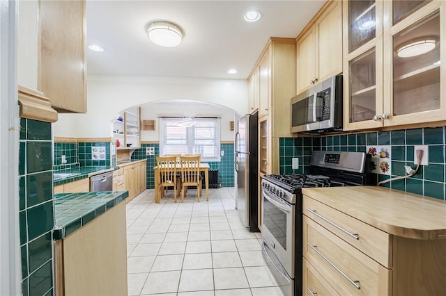 108 Iroquois St, Rochester, NY 14609 - kitchen featuring appliances with stainless steel finishes, tile walls, light brown cabinetry, tile counters, and arched walkways
