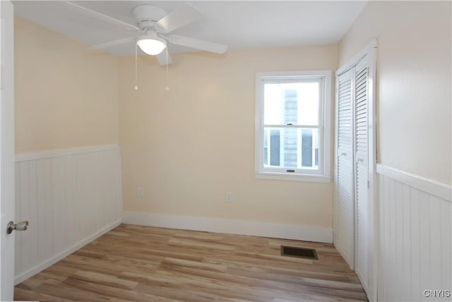 32 Franklin St, Champion, NY 13619 - unfurnished bedroom featuring light wood-style floors, a wainscoted wall, ceiling fan, and a closet