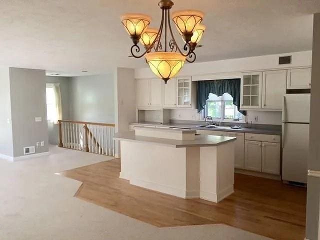 1369 Pittsford Mendon Rd, Mendon, NY 14506 - kitchen featuring freestanding refrigerator, glass insert cabinets, a chandelier, wood finished floors, and a center island
