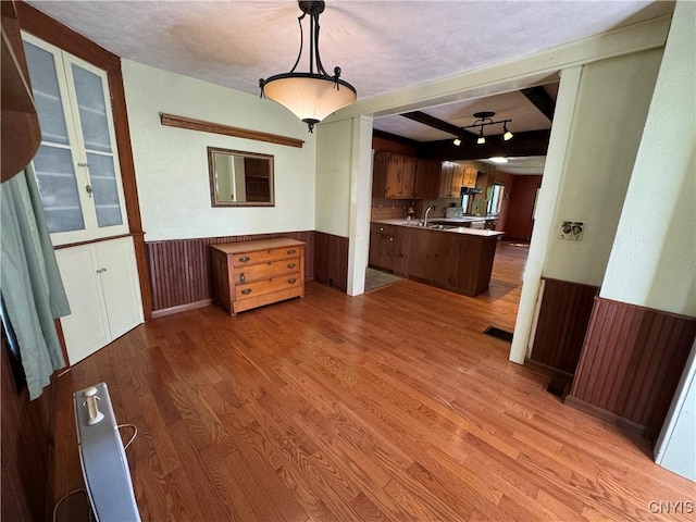 237 E Hamilton Ave, Sherrill, NY 13461 - kitchen featuring wainscoting, light wood-style flooring, glass insert cabinets, light countertops, and beamed ceiling