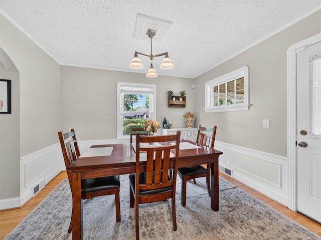 245 Worthington Rd, Irondequoit, NY 14622 - dining room with ornamental molding, light wood-type flooring, arched walkways, a wainscoted wall, and a textured ceiling