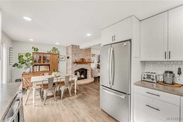 7052 Waring Cir, Evans, NY 14047 - kitchen featuring freestanding refrigerator, white cabinetry, a brick fireplace, light wood-type flooring, and tasteful backsplash