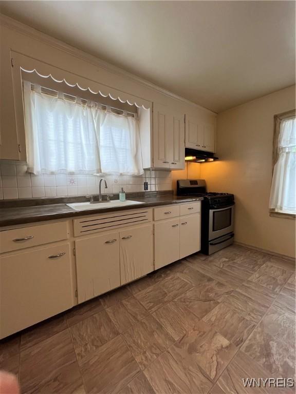 2479 Forest Ave, Niagara Falls, NY 14301 - kitchen with stainless steel gas stove, dark countertops, under cabinet range hood, white cabinets, and backsplash