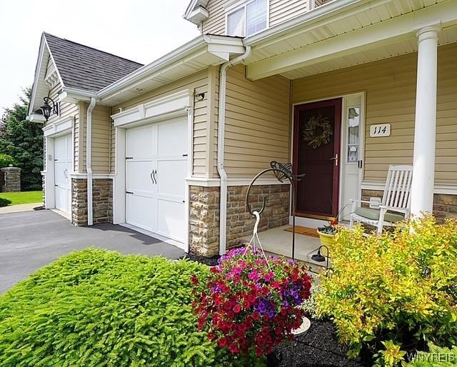 114 Slate Bottom Dr, Lancaster, NY 14043 - entrance to property featuring covered porch, stone siding, a shingled roof, and a garage