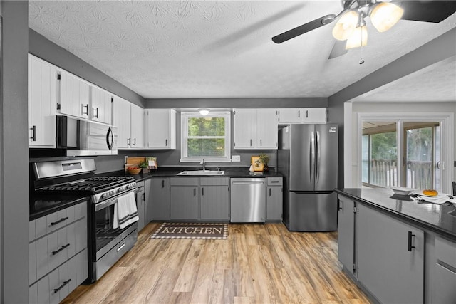 911 Copperkettle Rd, Webster, NY 14580 - kitchen with appliances with stainless steel finishes, dark countertops, light wood-style floors, white cabinets, and a ceiling fan