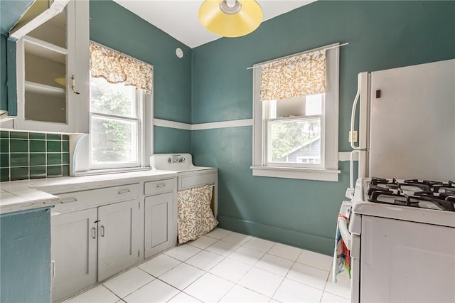 1085 Garson Ave, Rochester, NY 14609 - kitchen with white appliances, tile counters, white cabinets, light tile patterned floors, and backsplash