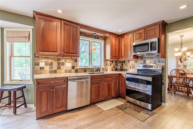15 Chesapeake Lndg, Henrietta, NY 14586 - kitchen featuring appliances with stainless steel finishes, light wood finished floors, brown cabinetry, light stone counters, and a chandelier
