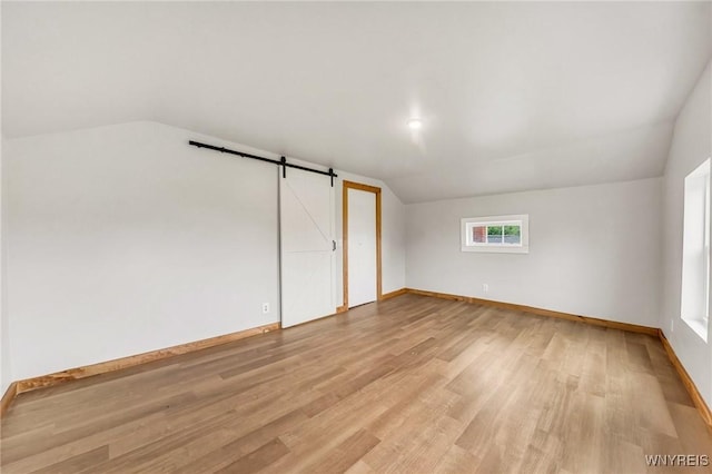 10655 Millers Rd, Yates, NY 14098 - unfurnished bedroom featuring vaulted ceiling, light wood-style flooring, and a barn door