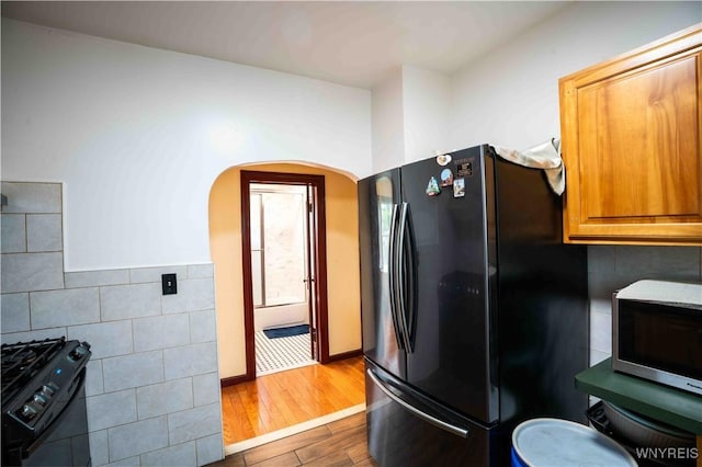 14 Phyllis Ave, Buffalo, NY 14215 - kitchen with black appliances, arched walkways, wood finished floors, tile walls, and brown cabinetry