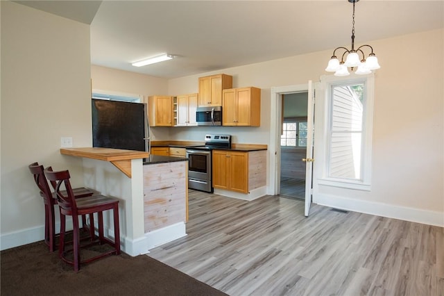 17 Orchard St, Canisteo, NY 14823 - kitchen with stainless steel appliances, a breakfast bar, dark countertops, a chandelier, and light wood-type flooring