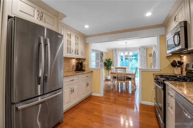 21 Towne Square Dr, Lancaster, NY 14086 - kitchen featuring appliances with stainless steel finishes, glass insert cabinets, light wood finished floors, tasteful backsplash, and a chandelier