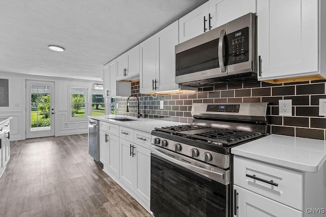 8953 Bushnell Shore Rd, Sullivan, NY 13037 - kitchen with appliances with stainless steel finishes, backsplash, wood finished floors, white cabinetry, and a textured ceiling